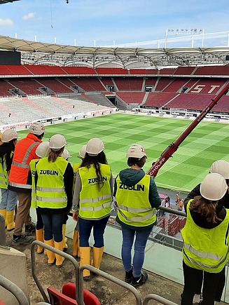 Kinder in Arbeitsschutzkleidung in der Mercedes-Benz Arena, von hinten zu sehen mit Blick aufs Fußballfeld.
