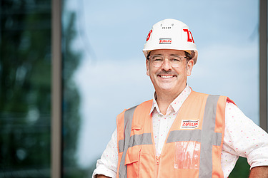 An employee wearing a hard hat and a high-visibility vest smiles at the camera.