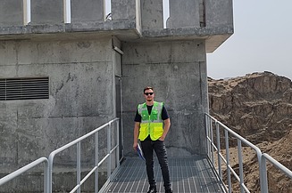 Junger Mann mit Warnweste steht vor einem Bauwerk.