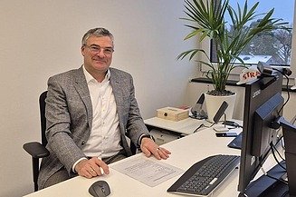 An employee is sitting at a desk in an office and smiling at the camera