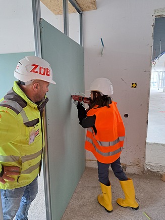 Mädchen in Arbeitsschutzkleidung bohrt in Wand.