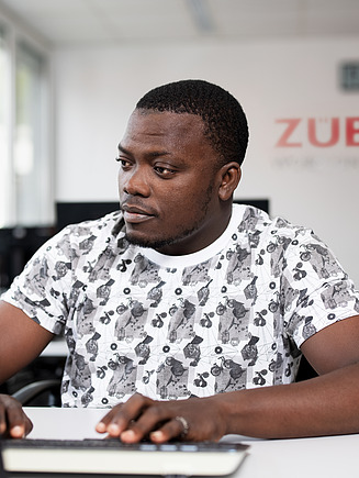 An apprentice is sitting at a computer, typing.