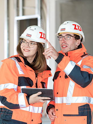 Foto von einer Frau und einem Mann auf der Baustelle, die ein Tablet in der Hand haben.