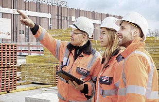 Foto von drei Personen auf der Baustelle stehen, wobei ein Mann mit dem Finger in die Ferne zeigt
