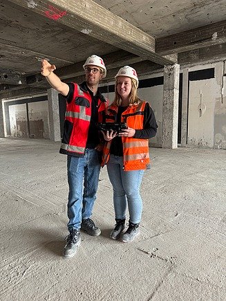 Zwei Mitarbeitende auf einer Baustelle, einer zeigt nach links