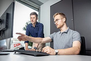 Two staff members in the office; one is pointing at a screen