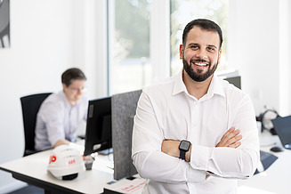 An employee is standing in the office, smiling at the camera
