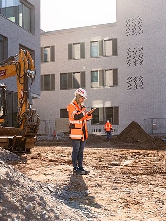 ZÜBLIN Mitarbeiterin mit PSA und Tablet auf einer Baustelle.