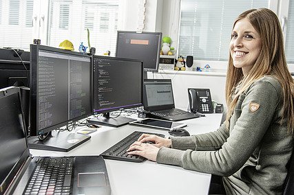 Foto von einer Frau, die in einen Computer mit mehreren Bildschirmen tippt