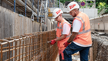 Zwei Mitarbeiter in Arbeitsschutzkleidung auf der Baustelle.