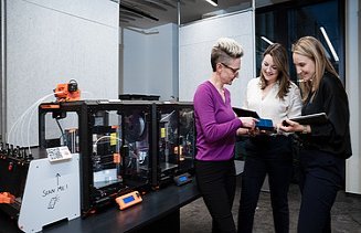 Drei ZÜBLIN Mitarbeiterinnen, die vor einem 3D Drucker stehen und etwas besprechen.