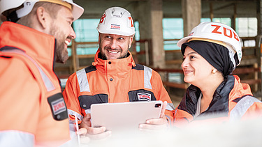 Zwei Mitarbeiter in Arbeitsschutzkleidung auf einer Baustelle in einer Besprechungssituation