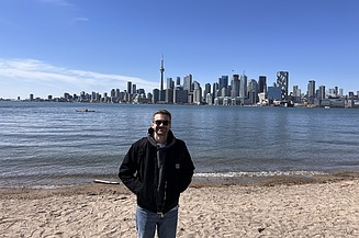 Junger Mann steht am Flussufer, im Hintergrund die Skyline von Toronto