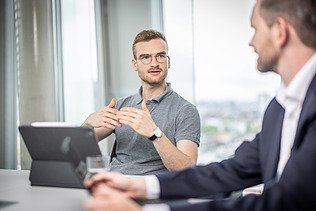 Zwei Mitarbeiter in einer Besprechung, einer mit Tablet gestikuliert