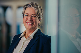 Vorständin Sabine Hahn lächelnd vor einem Bücherregal