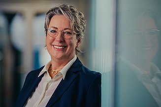 Vorständin Sabine Hahn lächelnd vor einem Bücherregal