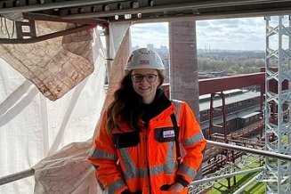 Bauleiterin Anica in Arbeitsschutzkleidung auf einem Gerüst mit einem Projekt im Hintergrund