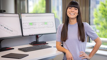 Foto einer ZÜBLIN-Architektin, die an ihrem Büroplatz mit Monitoren in die Kamera lächelt.