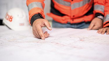 Nahaufnahme: Mitarbeiter zeigt auf Bauplan