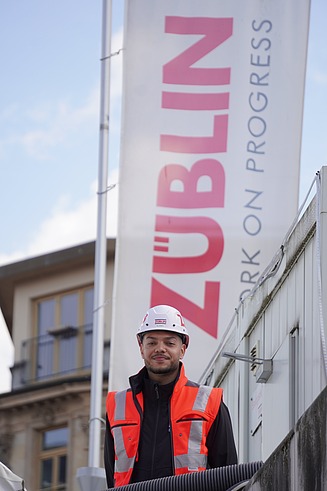 Joshua in Arbeitssicherheitskleidung vor einem ZÜBLIN-Banner