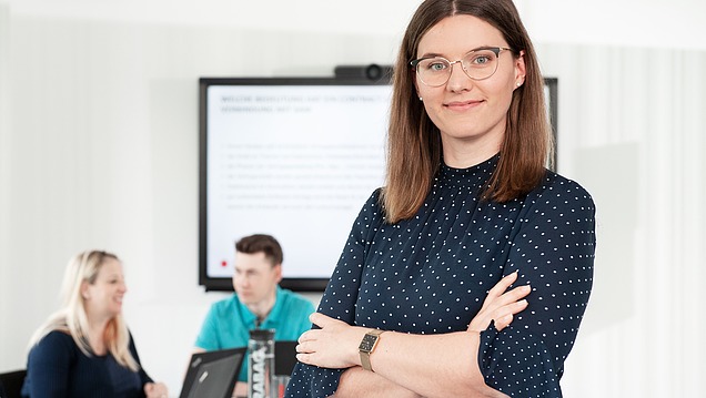 Junge Frau in einem Besprechungsraum mit verschränkten Armen.