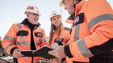 Foto von drei ZÜBLIN-Mitarbeitenden, die in einer Runde auf der Baustelle stehen und etwas besprechen.