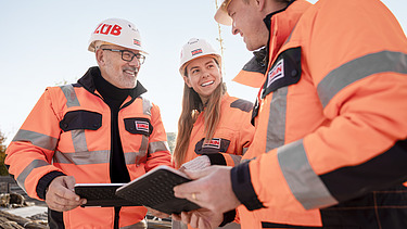 A photo of three ZÜBLIN employees standing in a circle on the building site, discussing something.