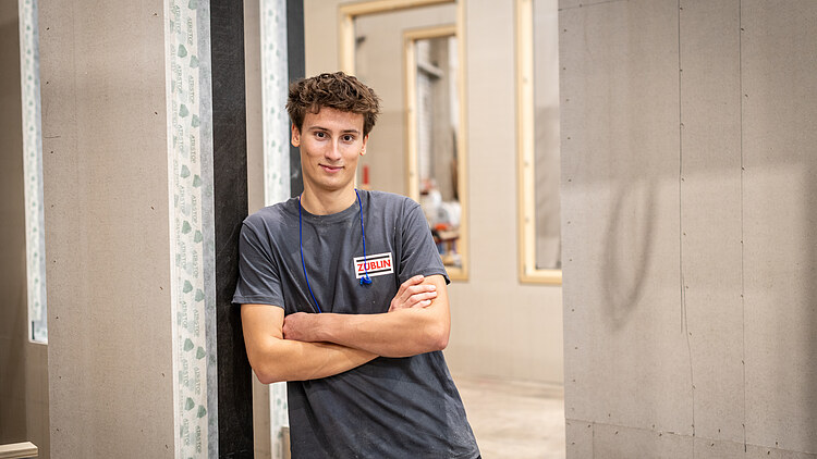 Mitarbeitender mit verschränkten Armen lehnend an Holzelementen