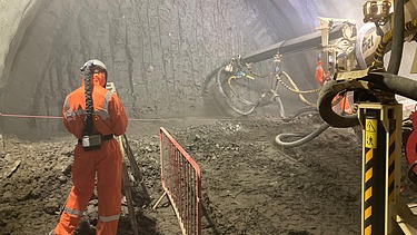 Foto eines Mitarbeiters auf einer Tunnelbaustelle neben einer Tunnelbohrmaschine.