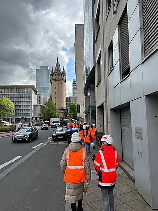 Kinder in Arbeitsschutzkleidung laufen auf dem Gehweg zu einer ZÜBLIN Baustelle.