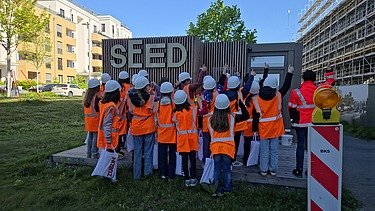 Kinder in Arbeitsschutzkleidung vor der Baustelle SEED
