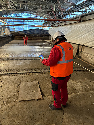 Mann in Arbeitsschutzkleidung und Tablet auf einer Baustelle (von hinten zu sehen)