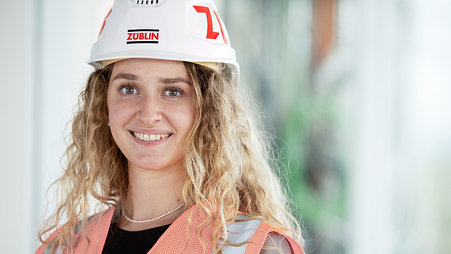 Junge Frau mit Bauhelm lächelt in die Kamera.