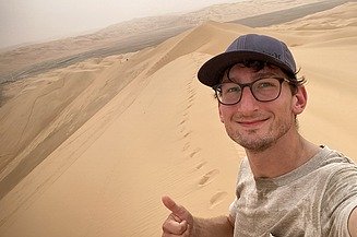Selfie eines jungen Mannes in der Wüste, zeigt den Daumen nach oben.