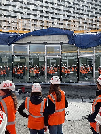 Kinder in Arbeitsschutzkleidung auf einer Baustelle, von hinten zu sehen. 