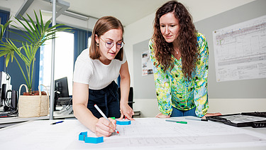 Two female staff members are discussing a building plan.