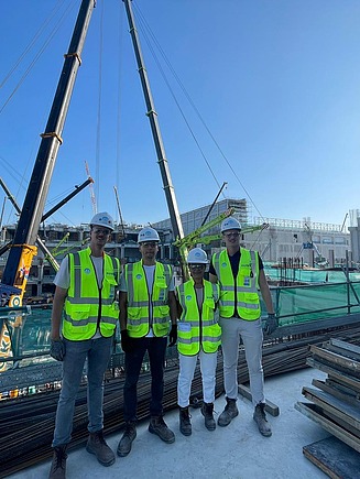 Vier junge Männer in Arbeitsschutzkleidung auf einer Baustelle.