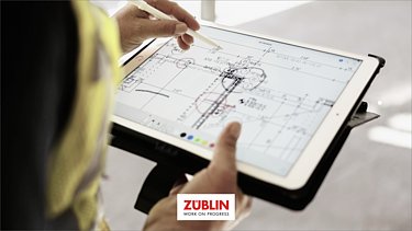 Foto von einem Tablet mit Bauplan, das von einem Mitarbeitenden gehalten wird,