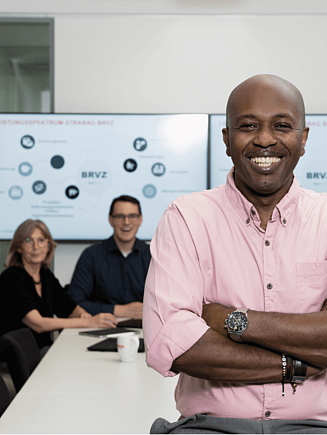 A man is standing in front of a conference table, smiling at the camera.