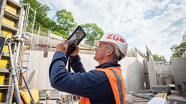 A man in high-visibility workwear on a building site, holding a tablet