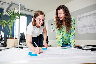 Two female staff members are discussing a building plan.