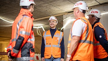 Vier Mitarbeiter in Arbeitsschutzkleidung auf einer Baustelle in einer Besprechungssituation