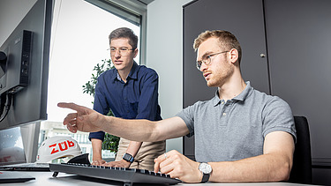 Two staff members in the office; one is pointing at a screen