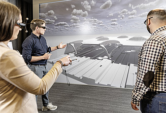 Drei Kolleg:innen stehen vor einer VR-Wand zusammen