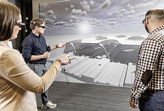 Three colleagues are standing together in front of a VR wall