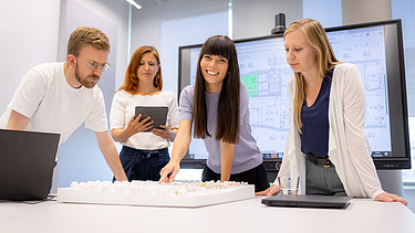 Four ZÜBLIN employees, leaning over a table together to discuss a plan.