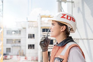 Foto von einer Auszubildenden mit Bauhelm und Funkgerät auf der Baustelle