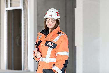 A young woman in high-visibility workwear holding a tablet on a building site