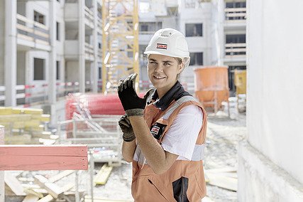 Foto von einer jungen Frau mit Helm auf eine Baustelle, die lächelnd die Kamera schaut