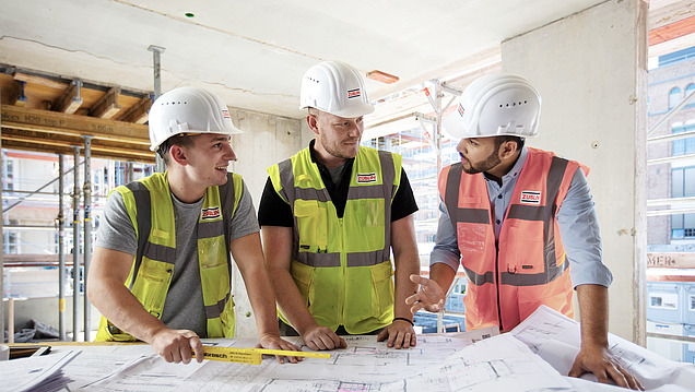 Drei Männer in Arbeitsschutzkleidung besprechen einen Bauplan.